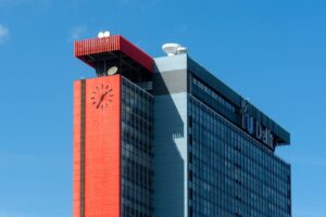 The modern facade and clock tower of TU Delft against a clear blue sky.
