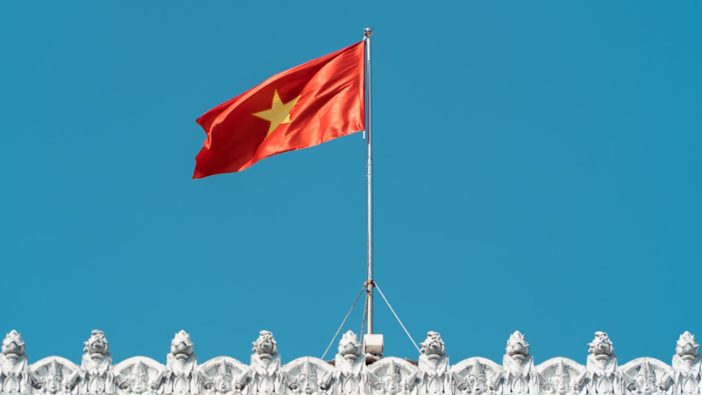 Vietnamese flag waving over an ornate white building against a clear blue sky.